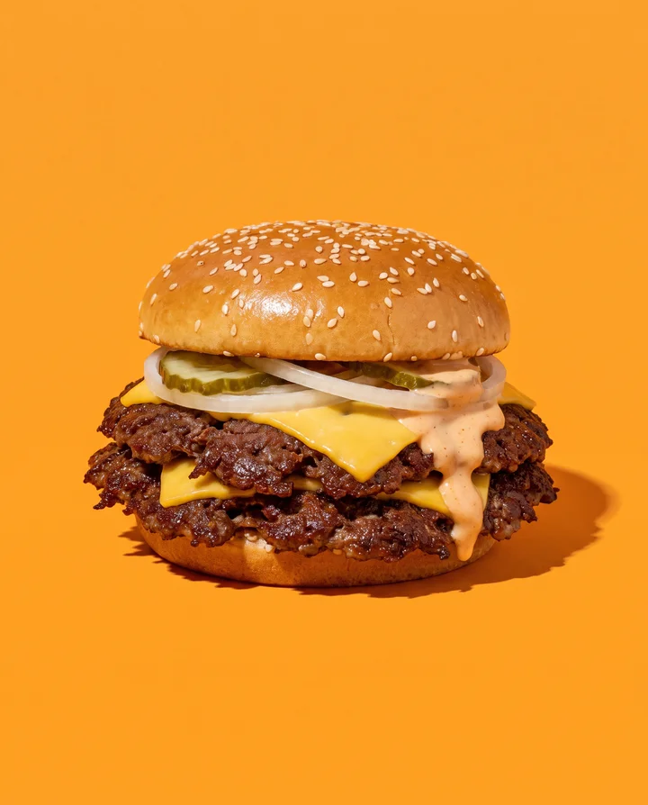 Der Doppelte: zwei Patties, zwei Scheiben Käse, Zwiebel, Gurke, Sauce läuft an der Seite herunter.